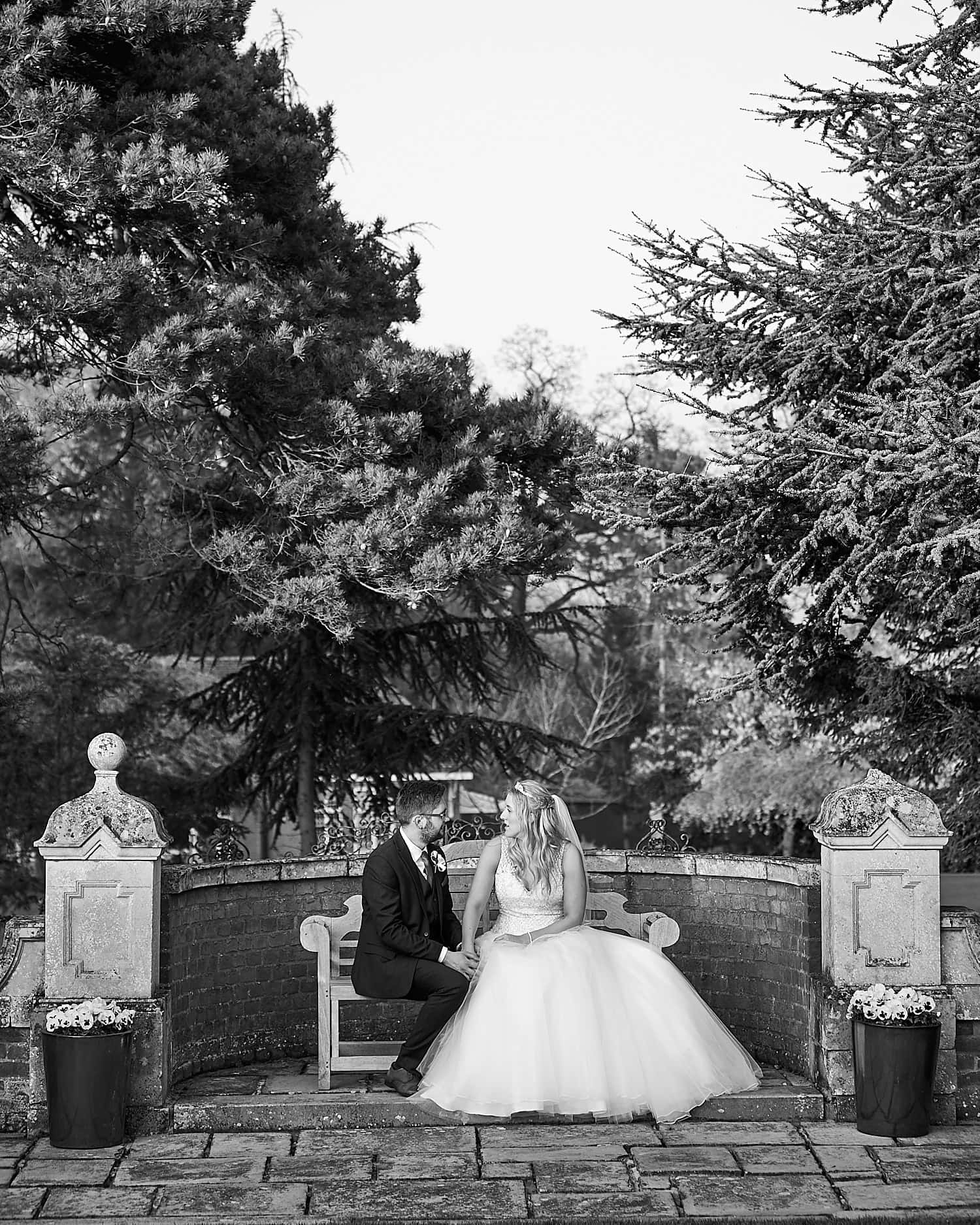 A couple chat on a bench during their wedding day. 