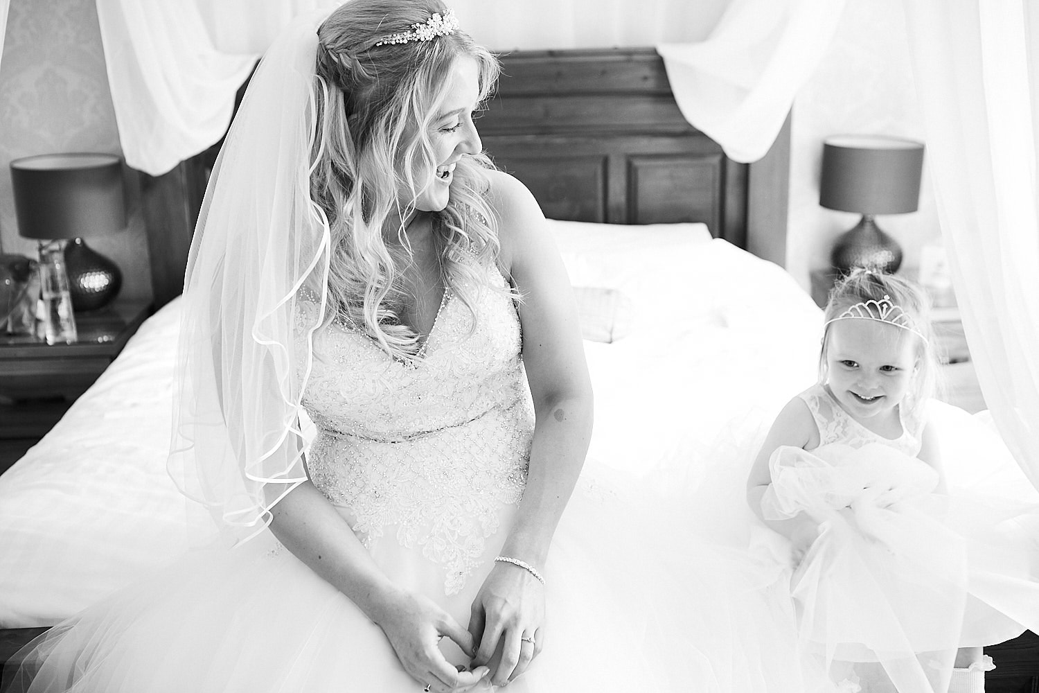 A bride and her flower girl sit on the bed