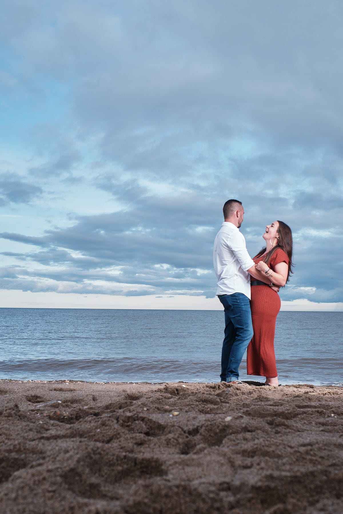 A couple laugh near the beach during their engagement photoshoot