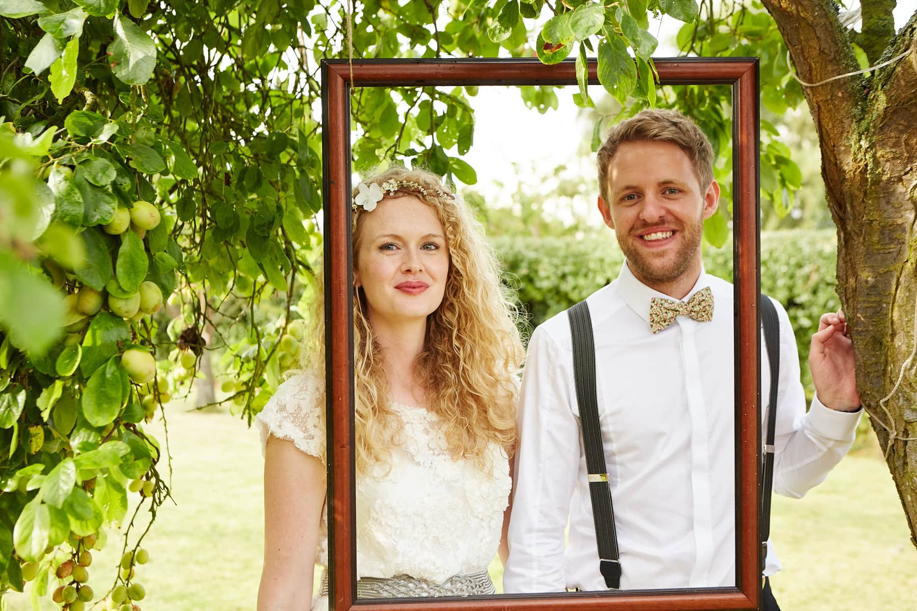 A couple pose in front of a picture frame hung from a tree in Spilsby on their wedding day.