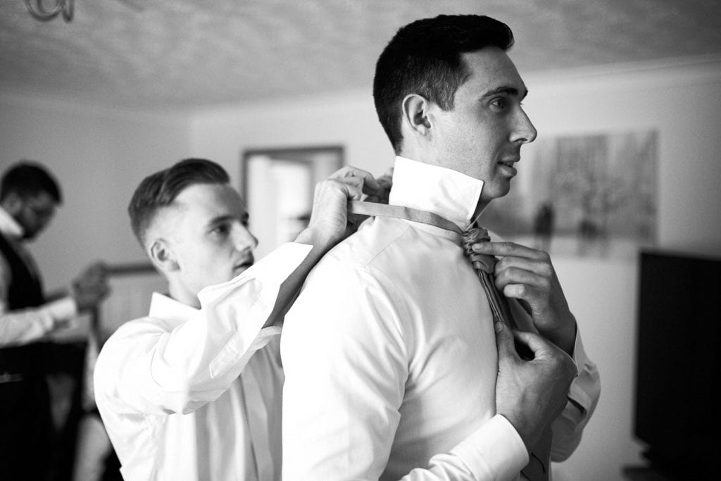 The best man helps the groom adjust his tie on the morning of his wedding.