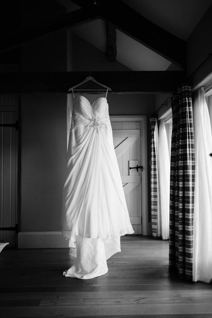 A black and white photo of a wedding dress hanging on the morning of a wolds wedding
