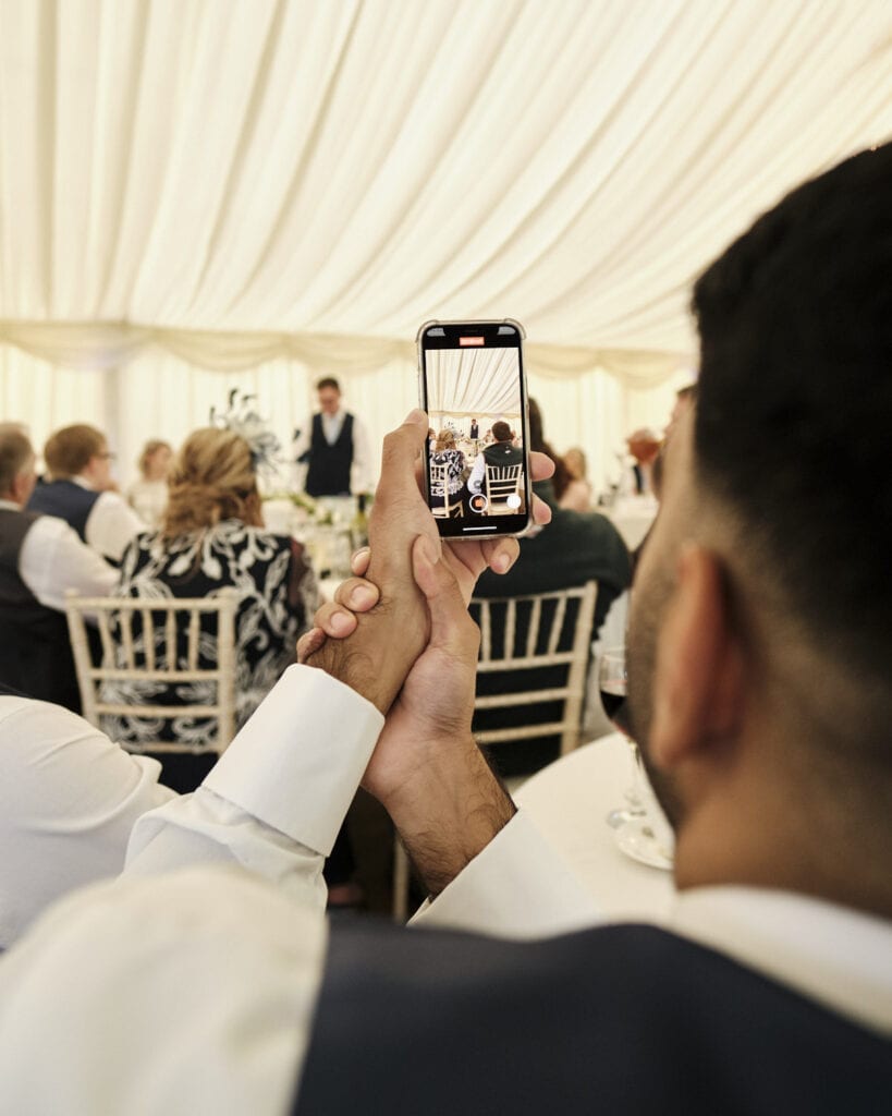 A Grooms speech being recorded by one of his friends on a beautiful summer wedding day.